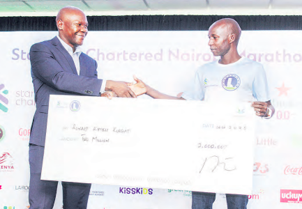 StanChart head of compliance David Mwindi (L) hands a dummy check to StanChart marathon champion Ronald Kurgat in Westlands, Nairobi on Tuesday. /TEDDY MULEI
