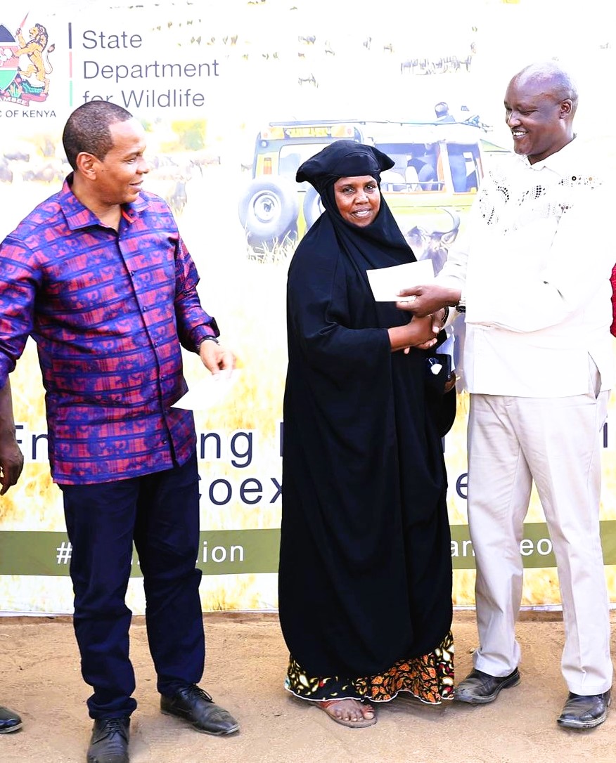Dr. John Chumo, the Conservation Secretary at the State Department for Wildlife hands over a cheque to a wildlife attack victim in Hola town. Looking on is Tana River Senator, Danson Mungatana.