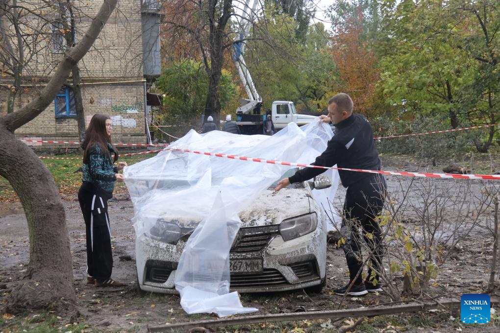 People cover a vehicle damaged in an airstrike with plastic sheeting in Kiev, Ukraine, on Oct. 25, 2025. One person was killed and 10 others were injured in Russian strikes on the Ukrainian capital overnight from Friday to Saturday, said a local official. (Photo by Peter Druk/Xinhua)